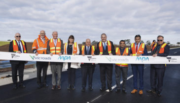 Collection of safety vest people behind a banner ribbon to celebrate the Sneydes Road opening