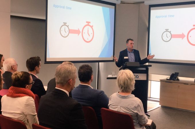 Photo of a presentation with people seated listening to speaker